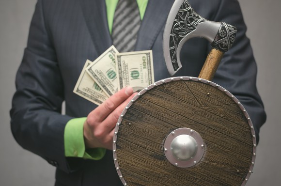 A businessman holding a Viking axe and shield and some money