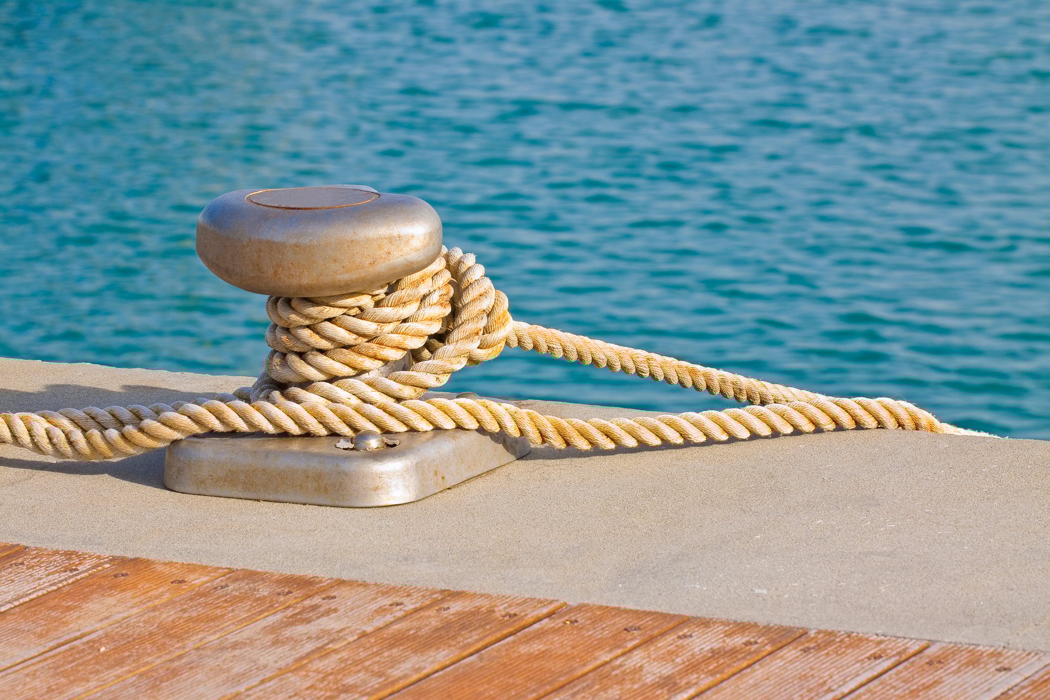 Close-up of a cleat for mooring boats with rope wrapped around it at waters' edge.