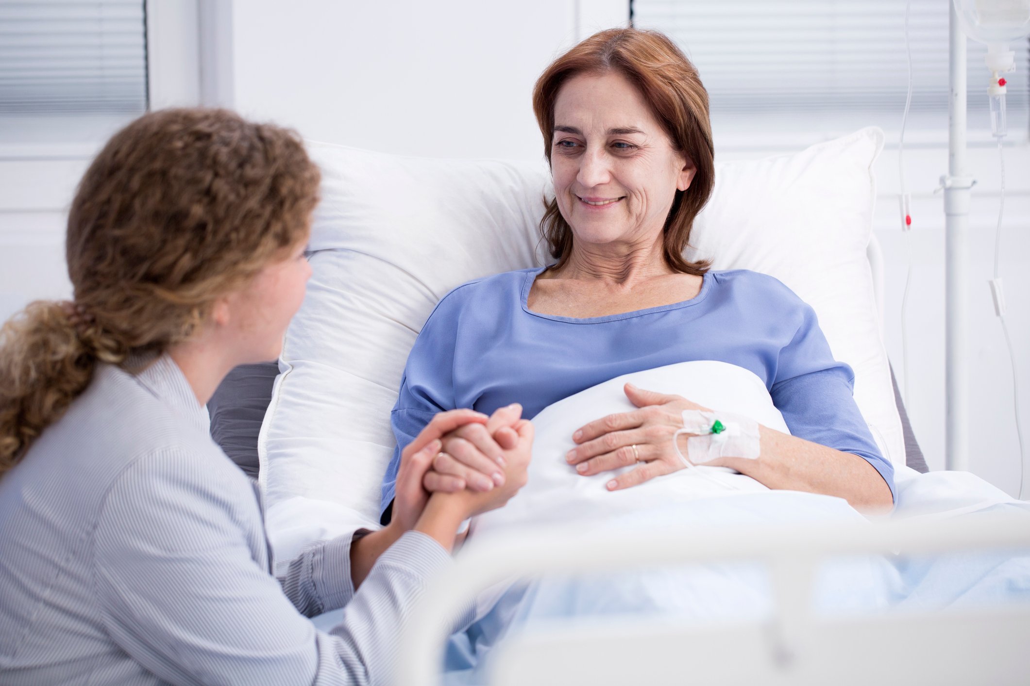 Woman in a hospital bed holding hands with another woman