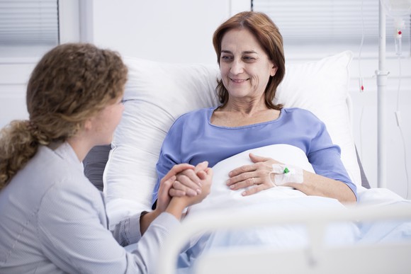 Woman in a hospital bed holding hands with another woman