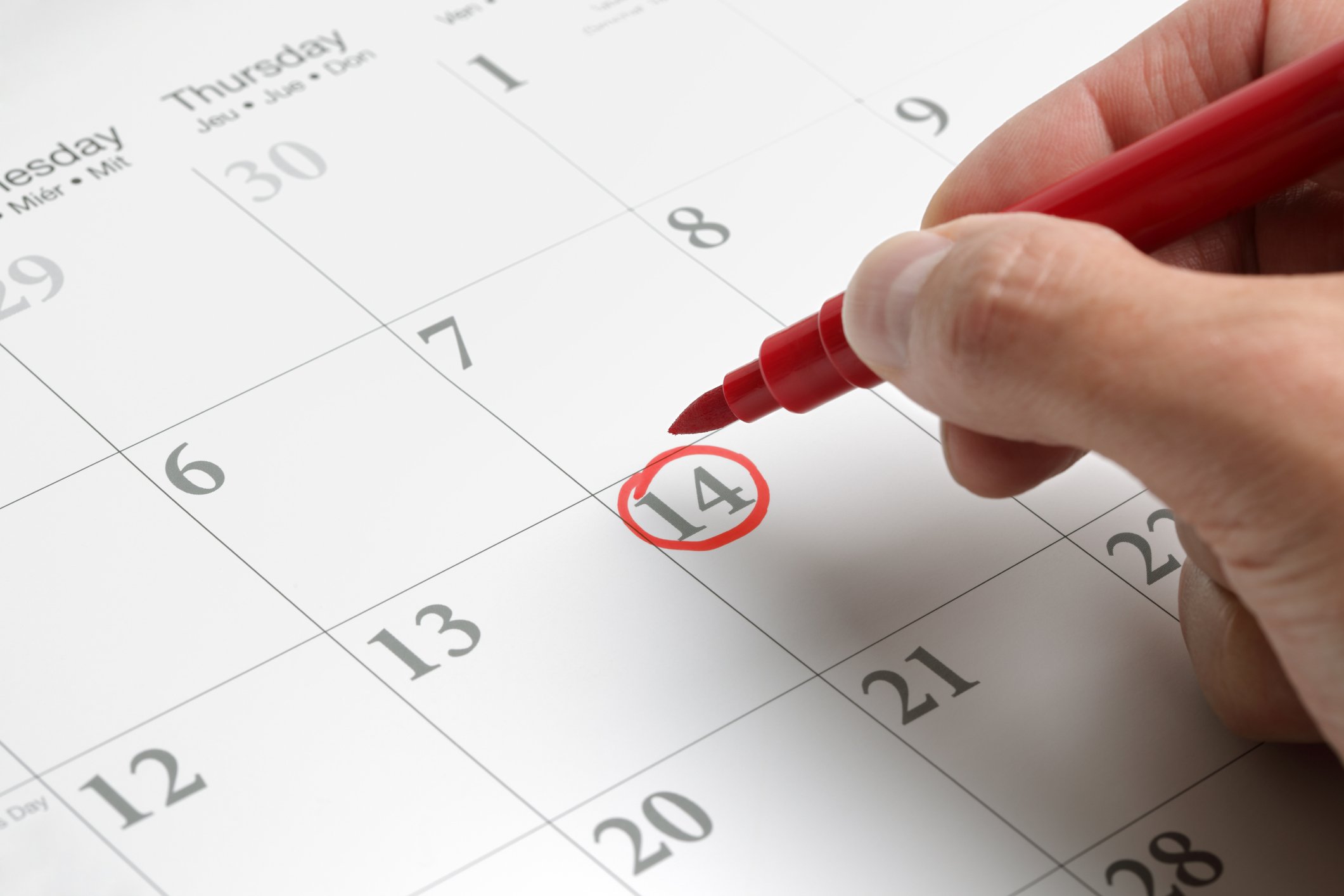 A person circling a date on a calendar with a red pen