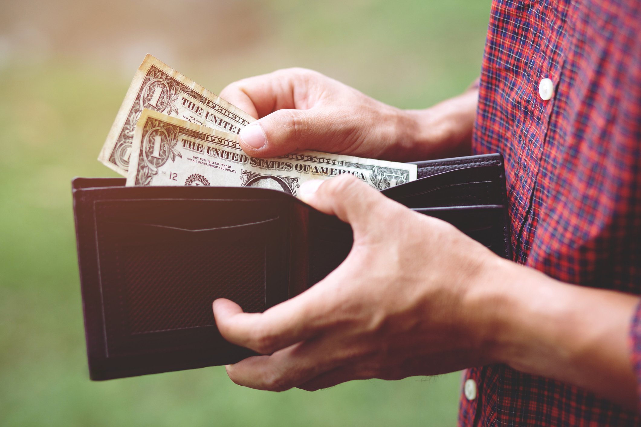 Close-up of a man pulling two one-dollar bills from a wallet.