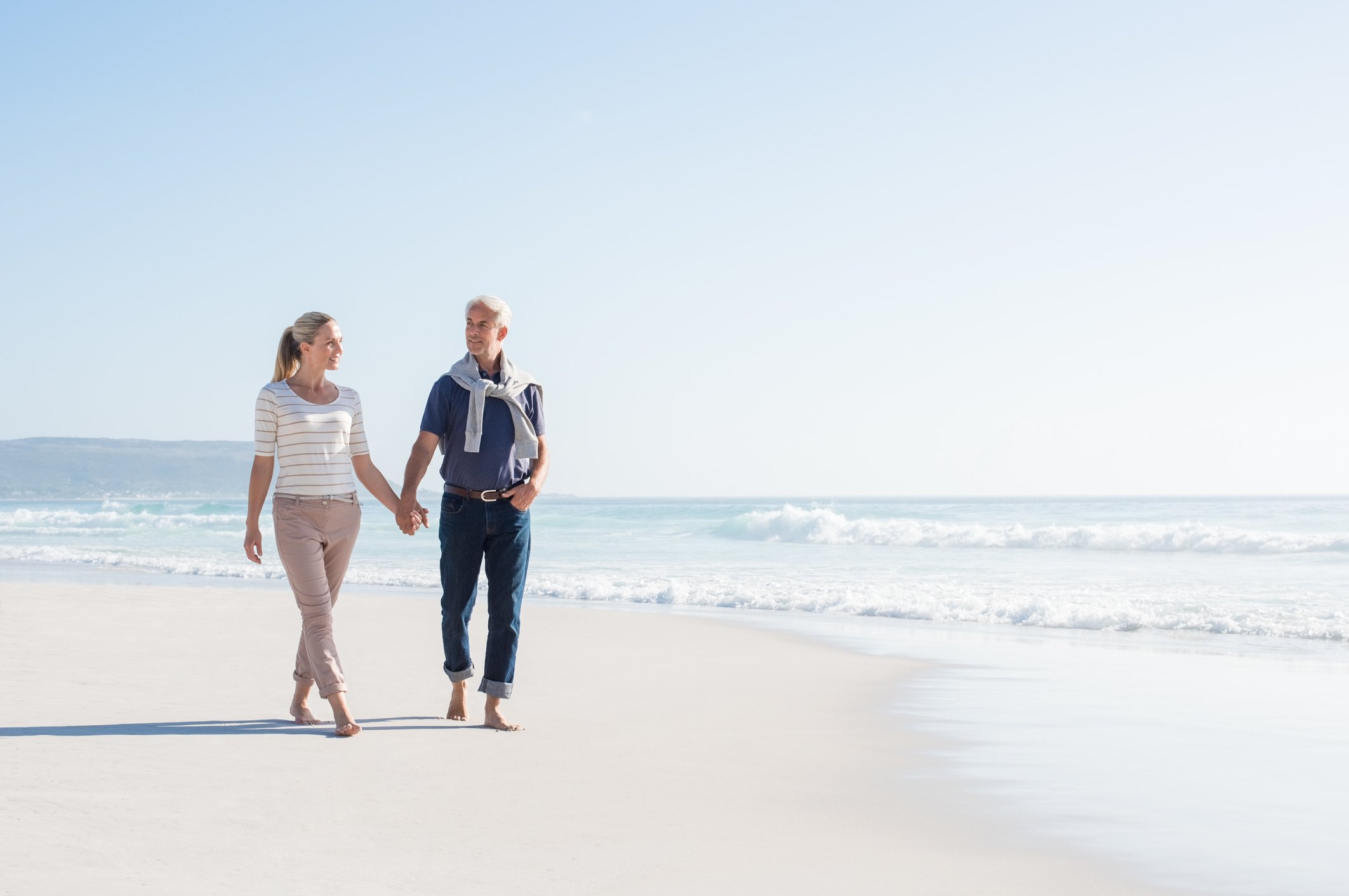 An older couple walks on a beach. 