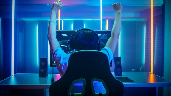 A gamer with his fists in the air, wearing a headset and playing a game on a PC.