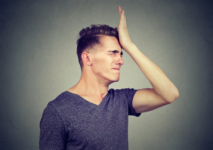 We see a young man slapping his forehead and wincing in regret. 