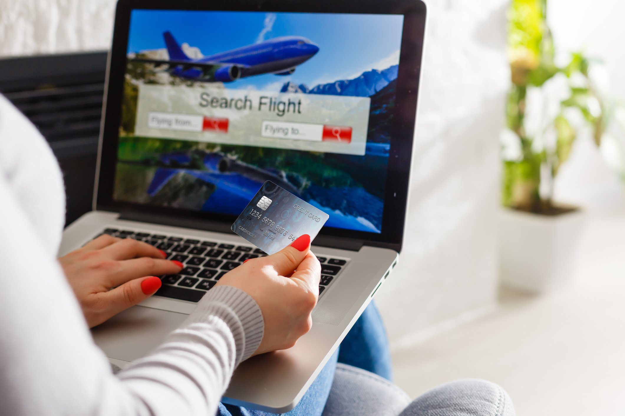 Woman with laptop is holding a credit card, booking a flight online.