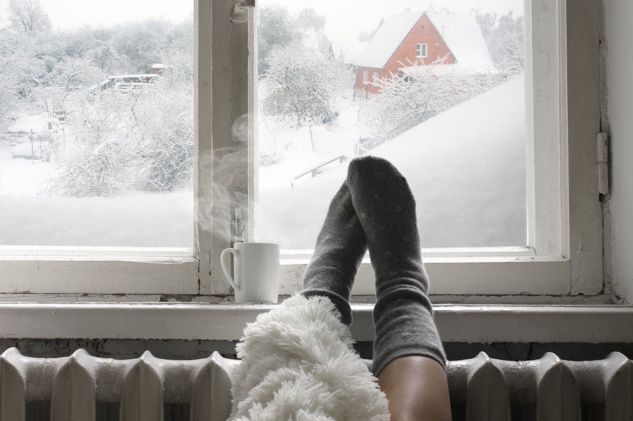 A pair of feet on a radiator in front of a window with snow outside