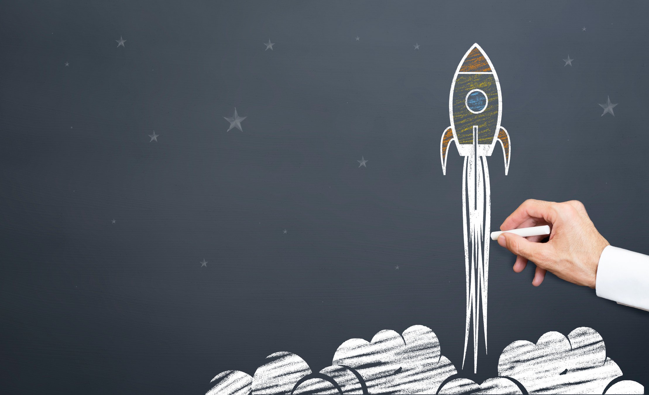 A man draws a rocket lifting off on a chalkboard.