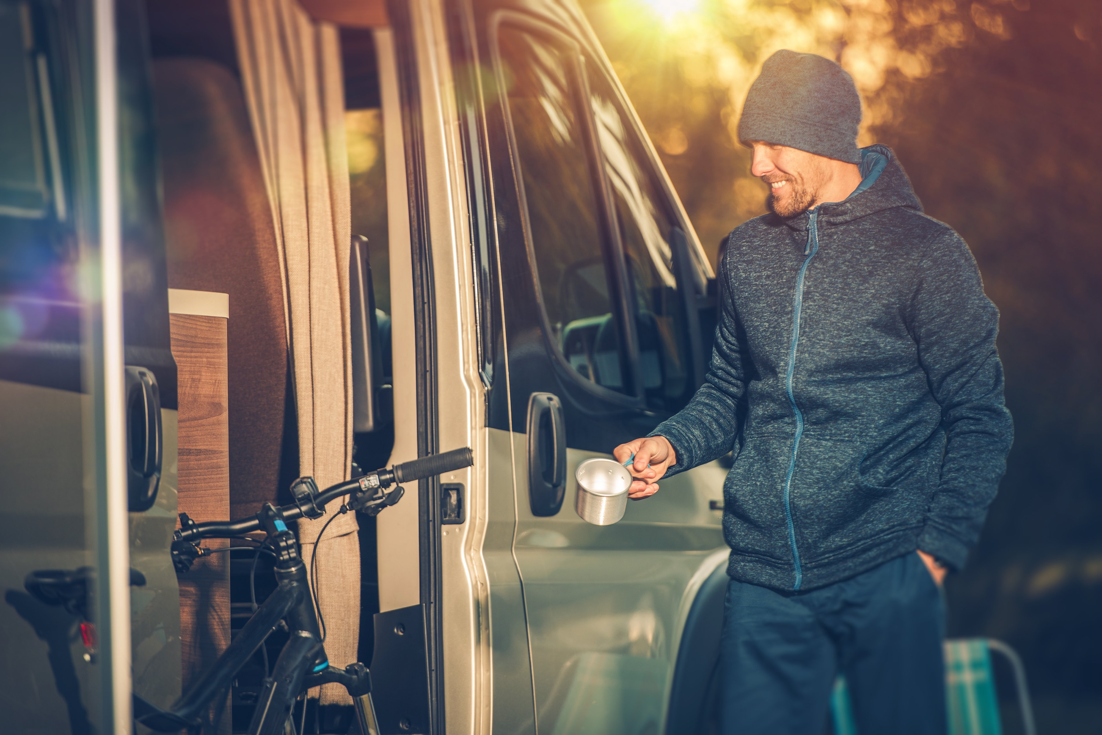 A man holds a cup of coffee and smiles outside his RV camper.