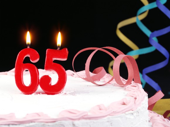 Candles in the shape of 65 burning on top of a frosted cake with streamers off to the side