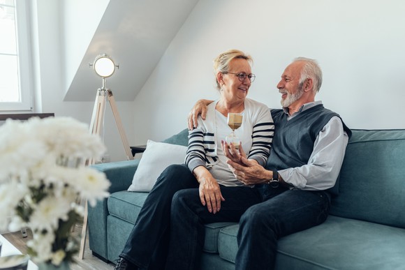 Older couple sitting on a couch, holding an hourglass.