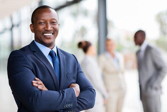 Smiling man in business suit with arms crossed and co-workers in background