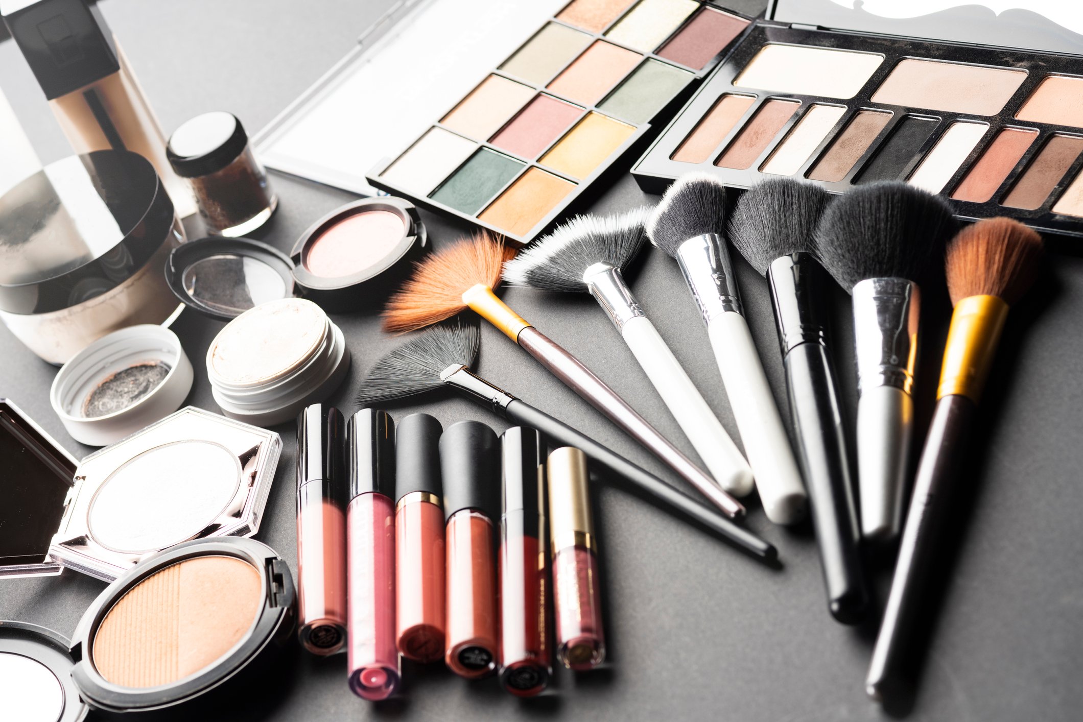 Multiple cosmetic products like makeup and brushes laid out on a flat surface.