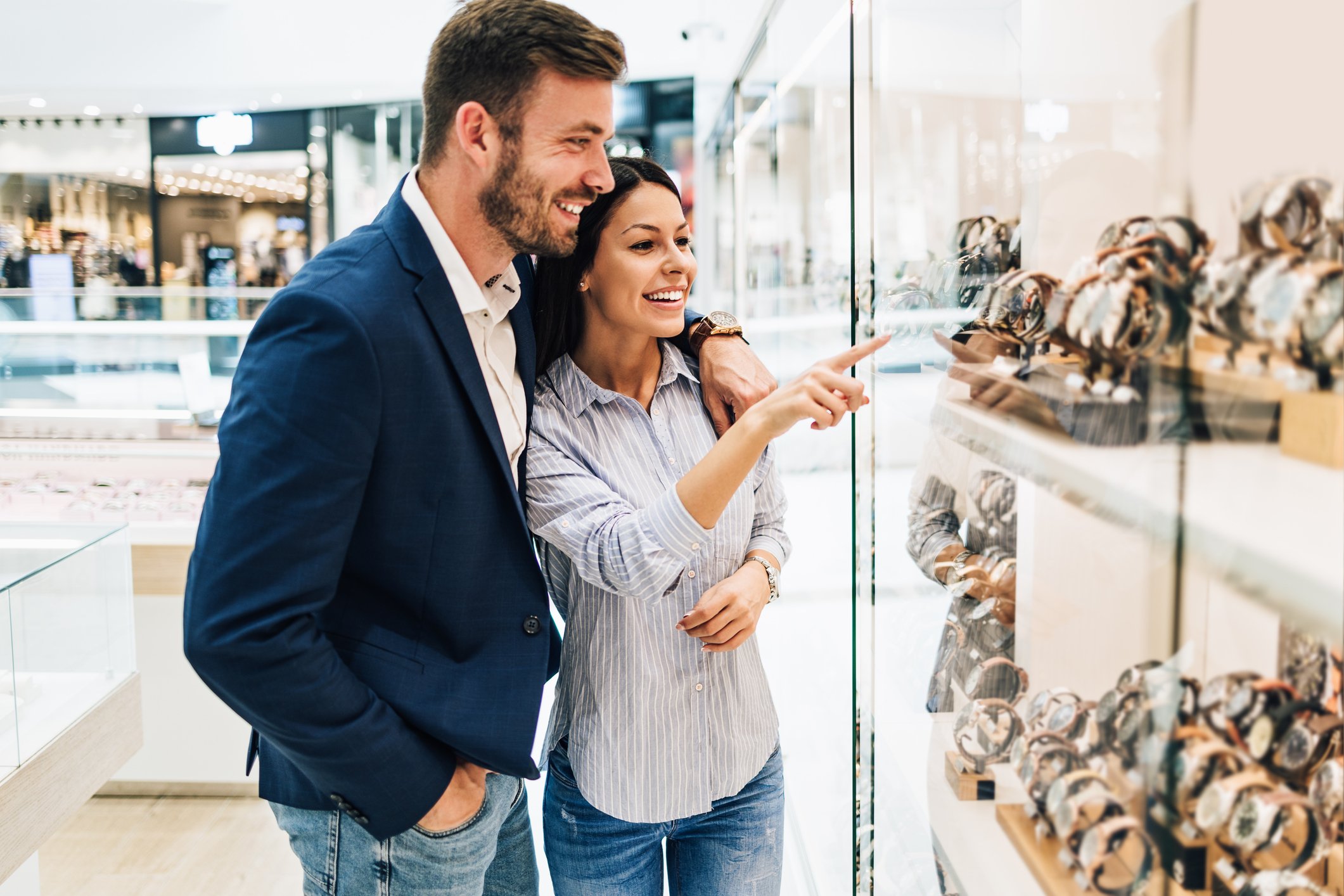 A man and woman in a jewelry store looking at a case of watches.