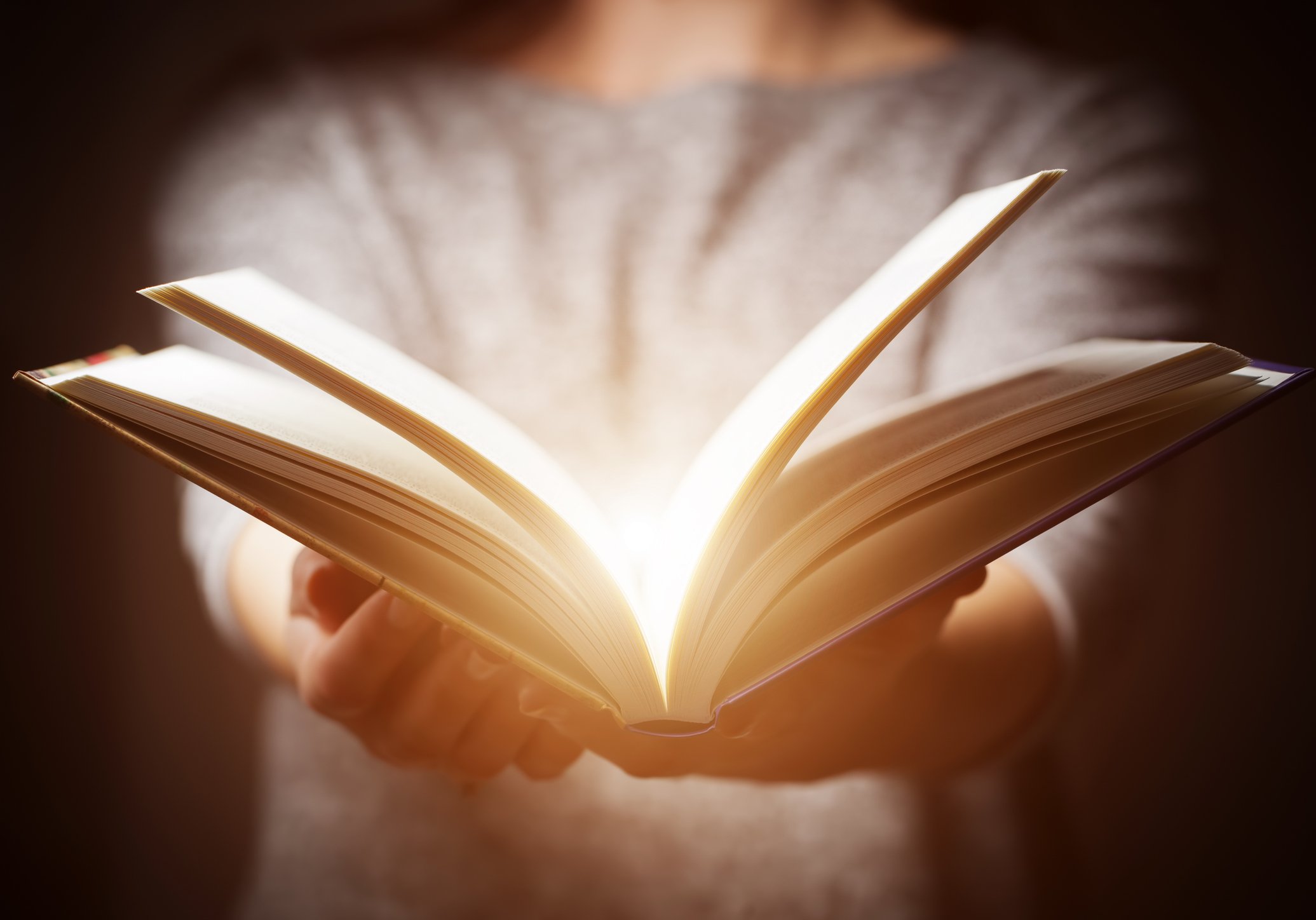 A person holding an open book with outstretched arms