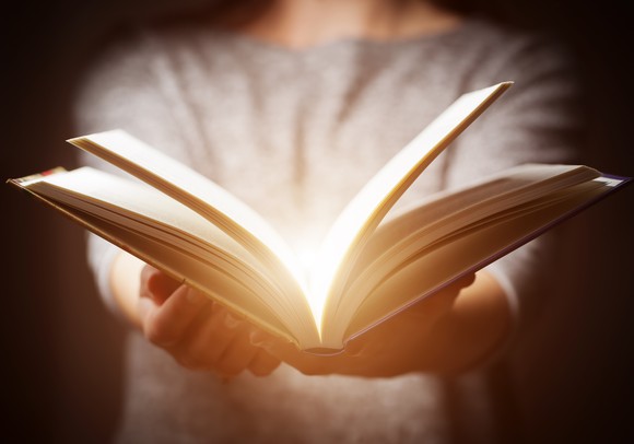 A person holding an open book with outstretched arms