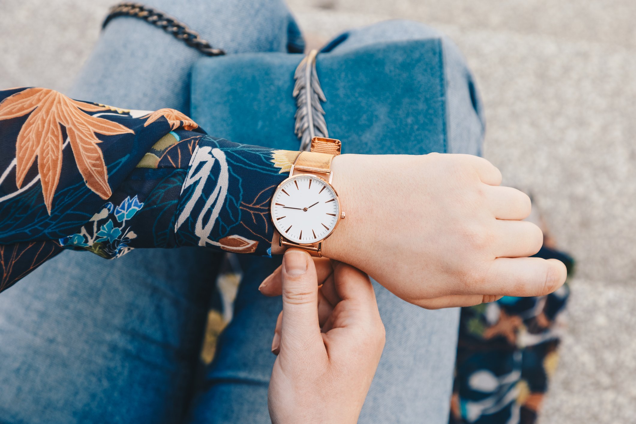 Close up of a woman in a floral shirt seated on stone steps, checking her watch.