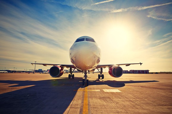 A commercial airplane on the tarmac, with the sun in the background.