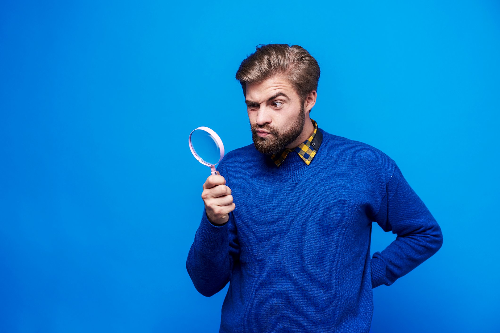 A bearded man looks through a magnifying glass