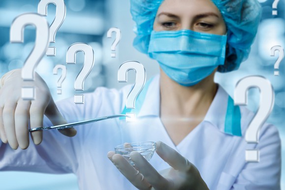 Doctor surrounded by question marks and grabbing a question mark with her clamp.