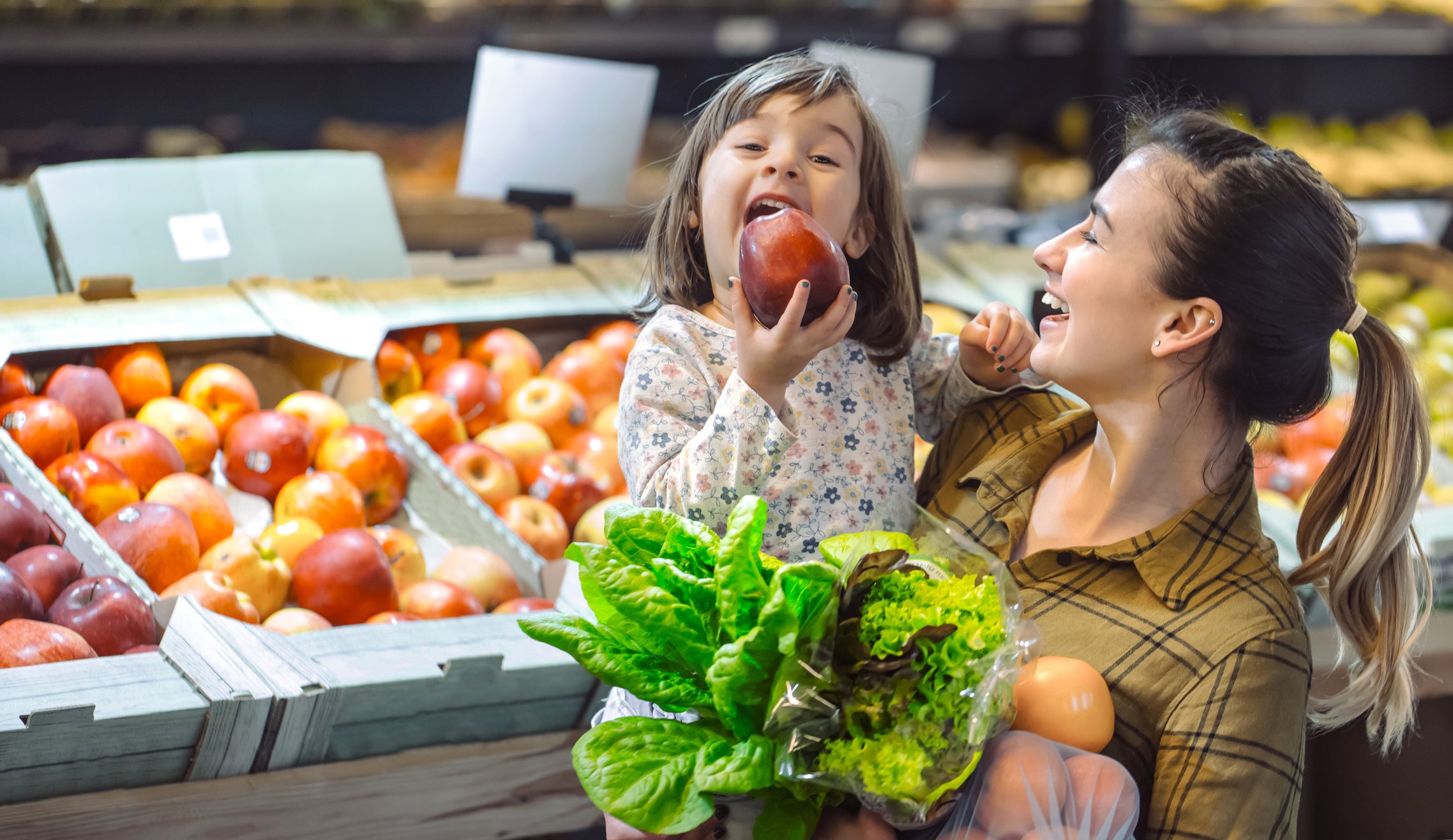 Woman shopping with a little girl who is eating an apple.