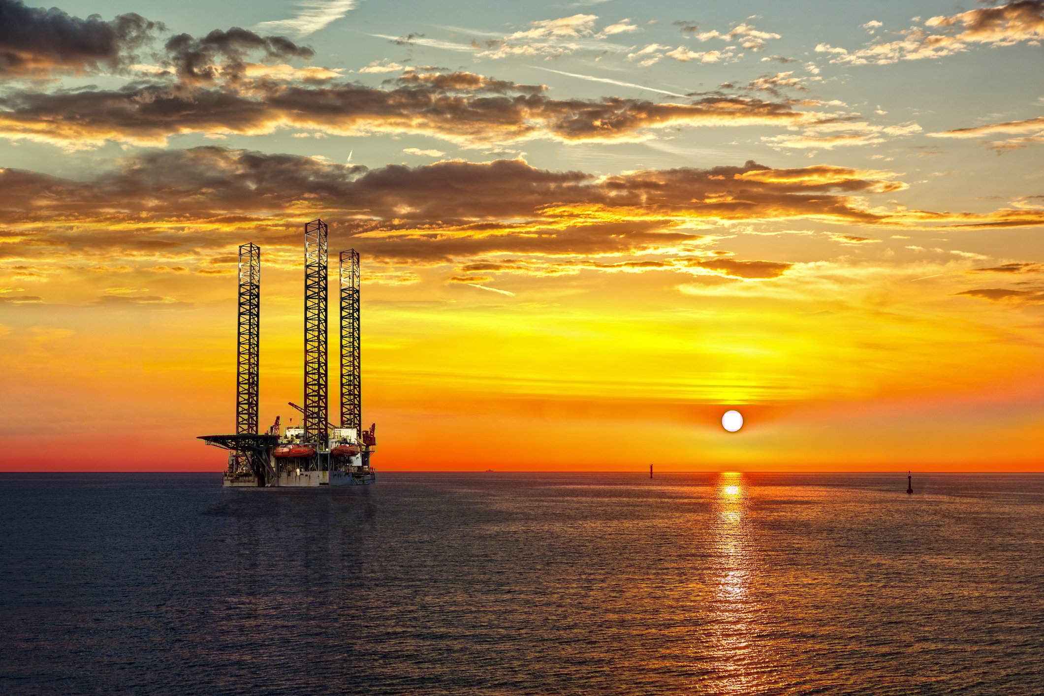 An offshore drilling rig with a bright sunset in the background.