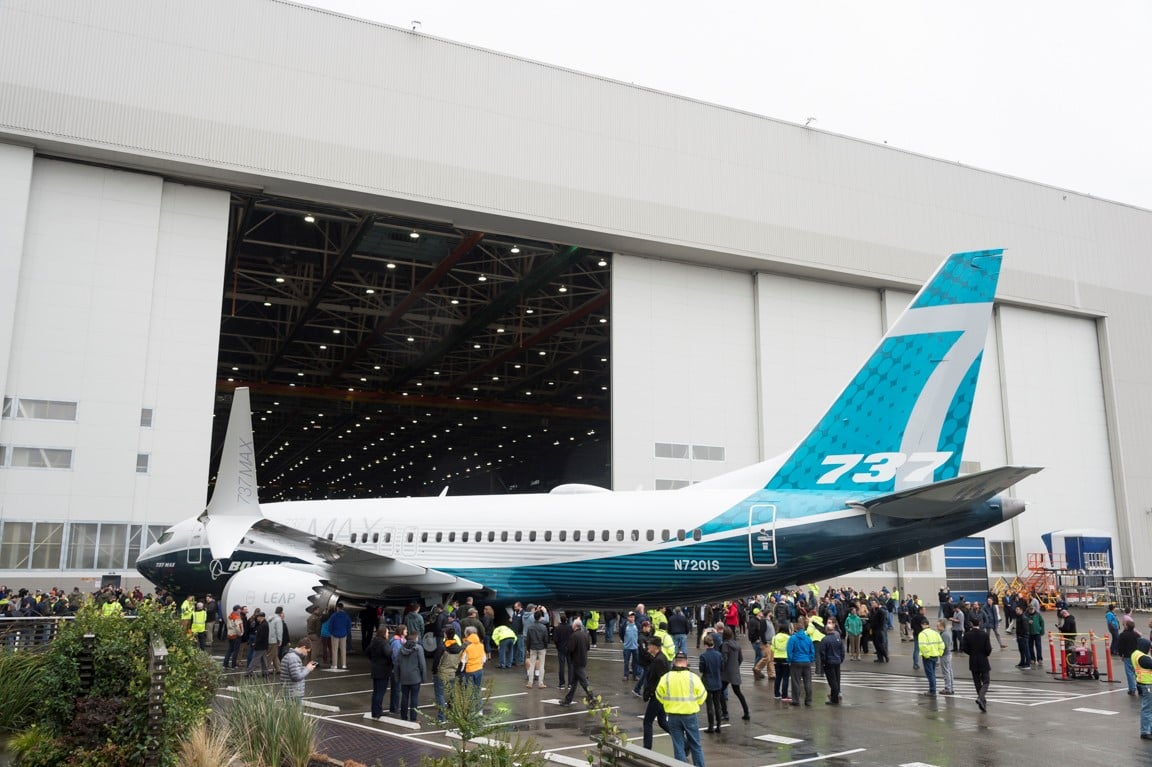 A Boeing 737 MAX next to a hanger surrounded by people.