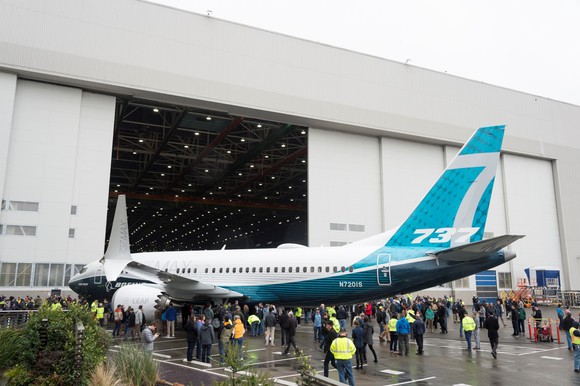 A Boeing 737 MAX next to a hanger surrounded by people.