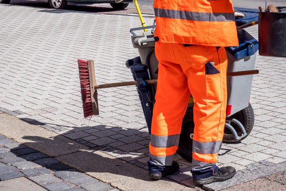 Street sweeper with broom in orange outfit