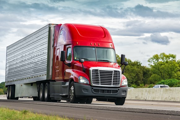 A red semi-truck barrels down the highway.