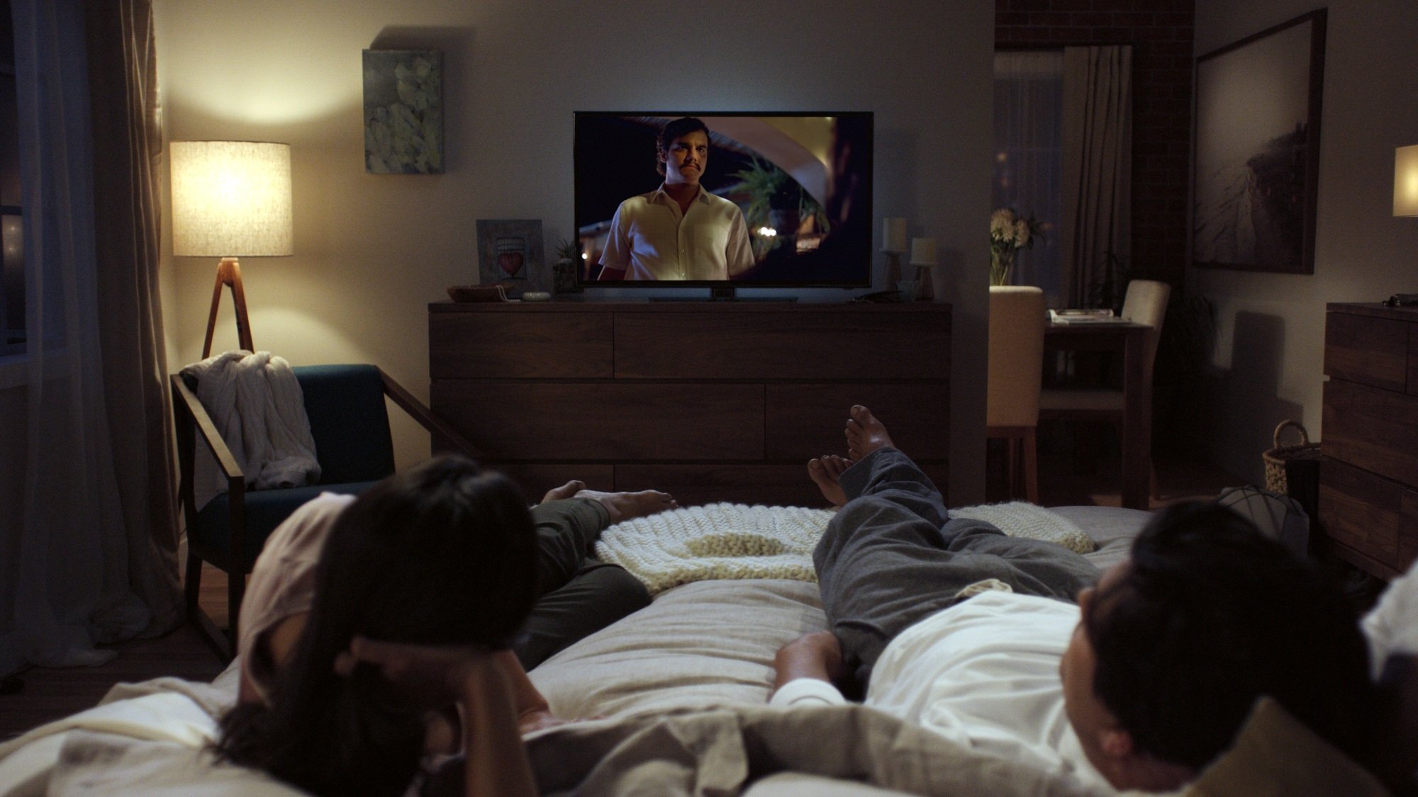Couple lying in bed watching Netflix show on television.