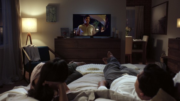 Couple lying in bed watching Netflix show on television.