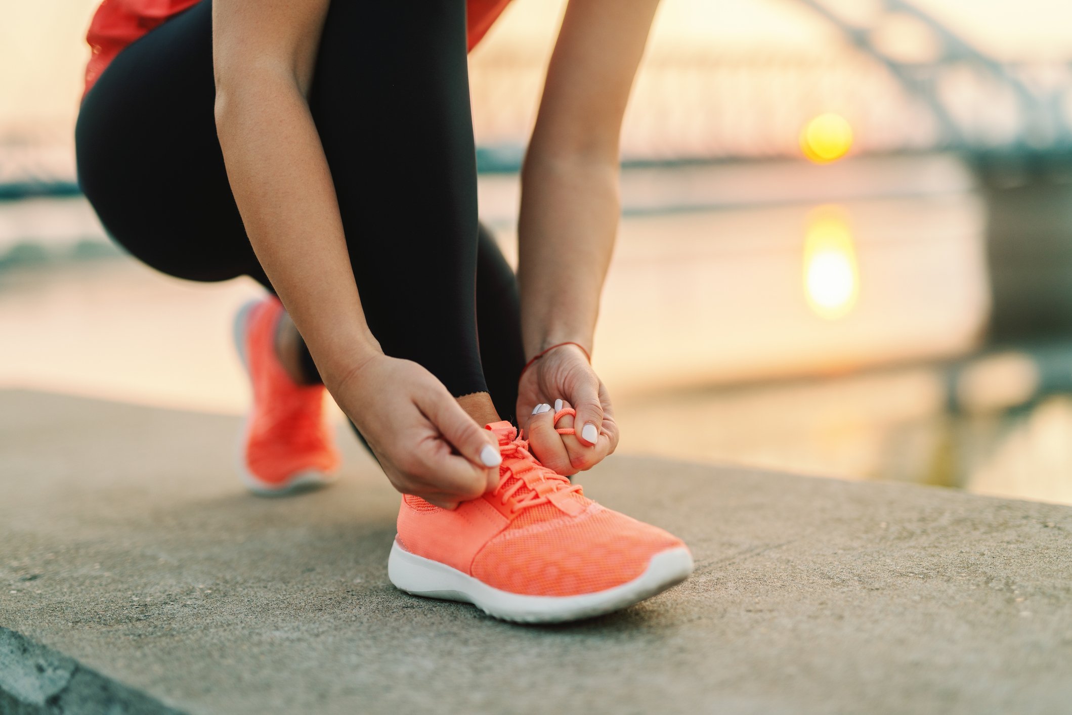 A person tying a running shoe outside as the sun rises