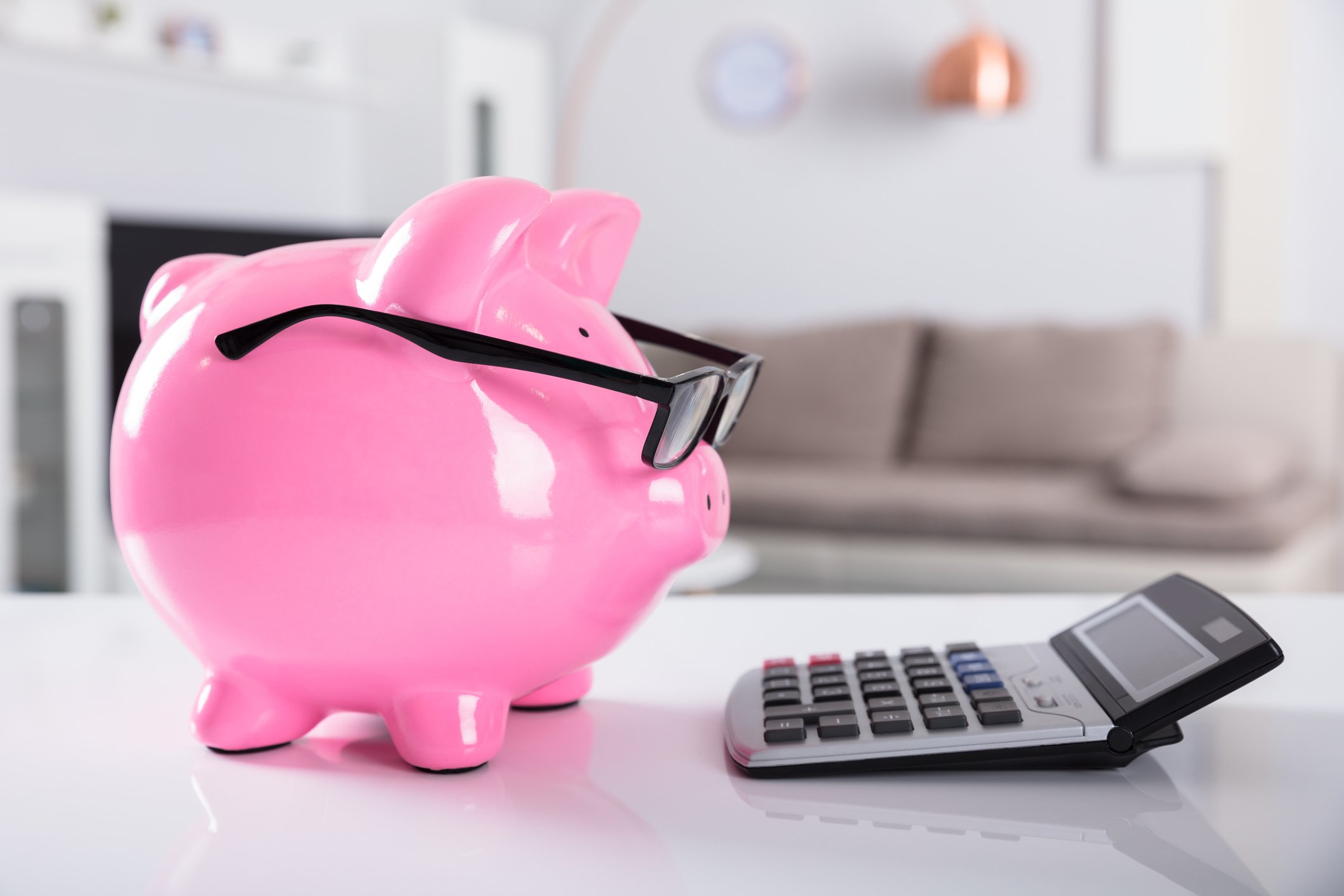 A piggy bank wearing glasses staring at a calculator.