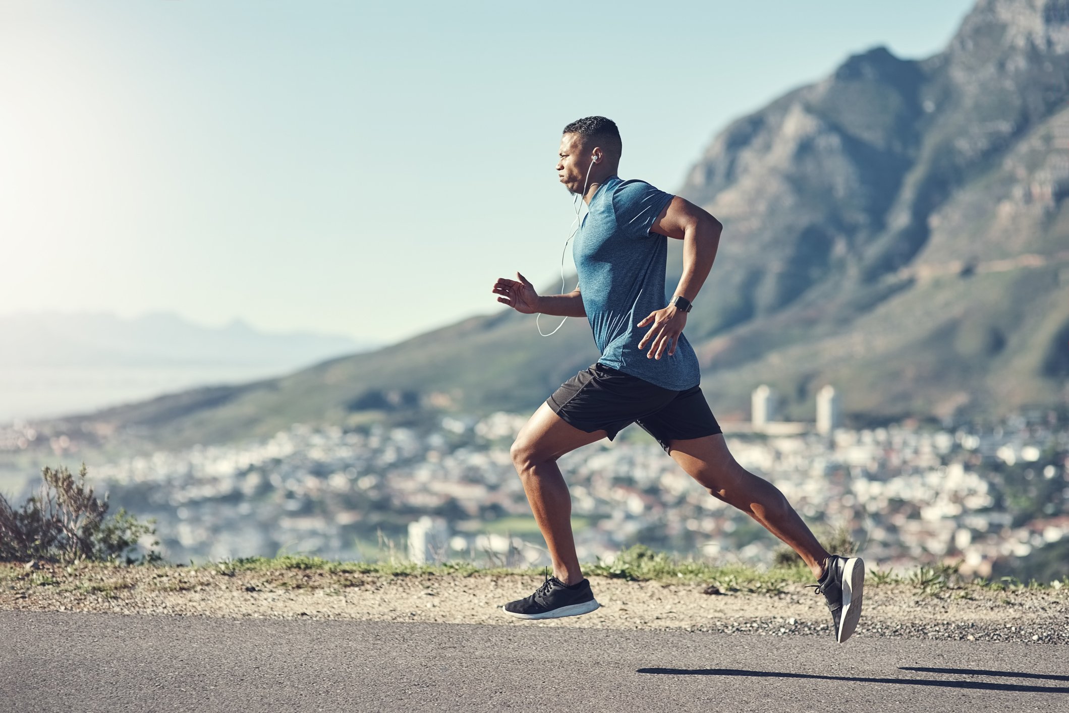 Man running in athletic gear and headphones, with mountains in the background.