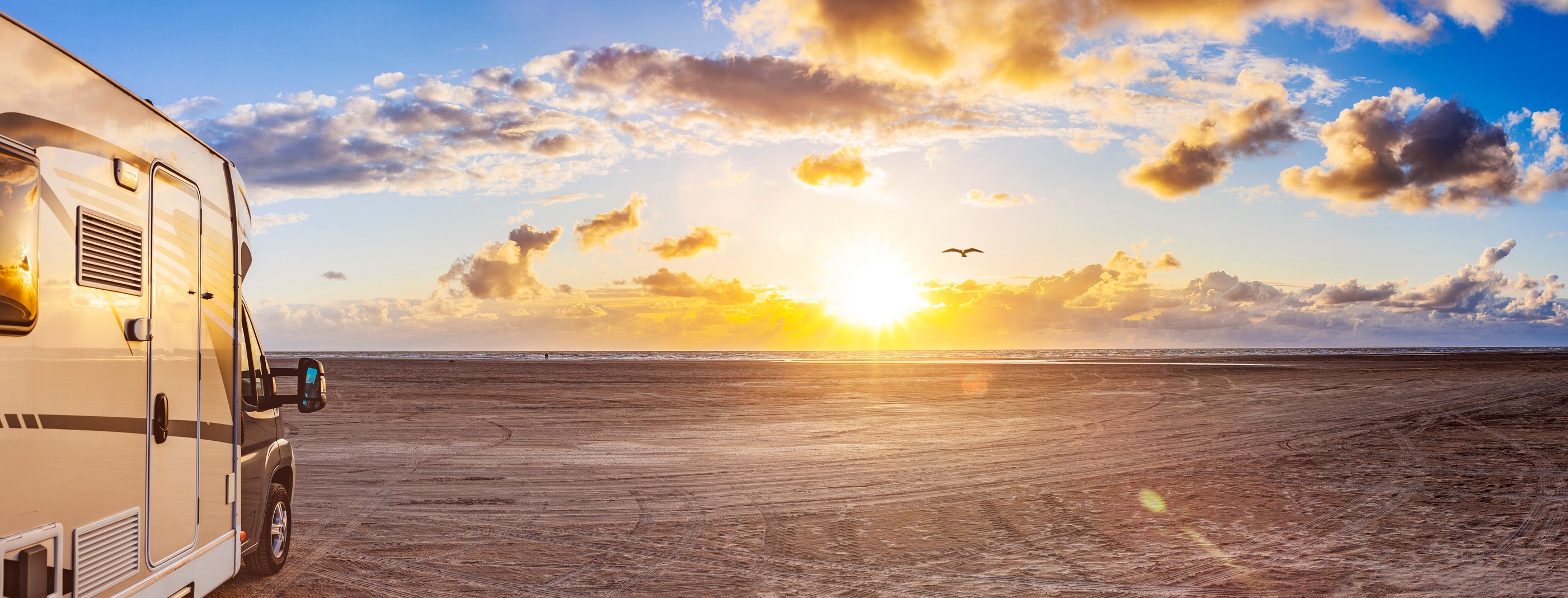 A recreational vehicle is parked on a beach at sunset.
