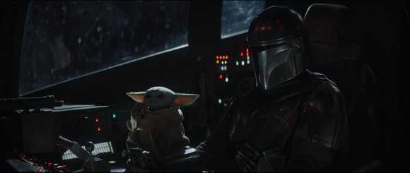 The Baby Yoda character and the Mandalorian sitting in the cockpit of a spaceship