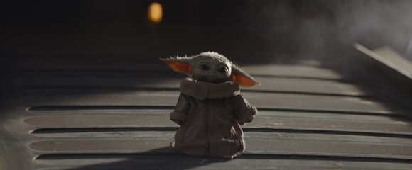 A small green creature with big ears wearing a robe, walking down a ramp