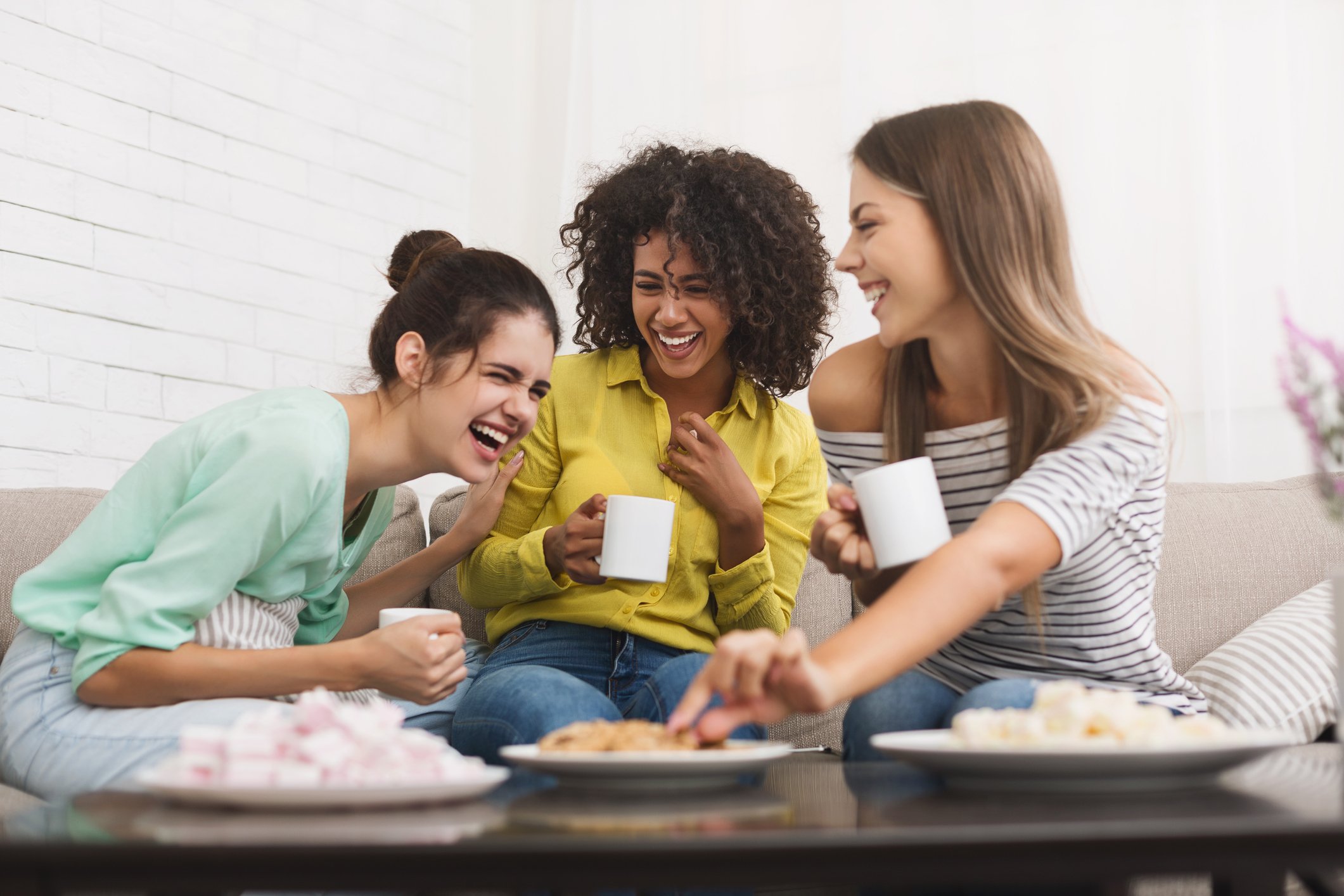 Three women happily laugh while drinking tea.