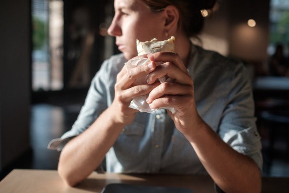 Man holding a burrito in has hand, looking out window of a quick service Tex-Mex restaurant.