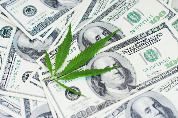 A cannabis leaf on top of a pile of $100 bills
