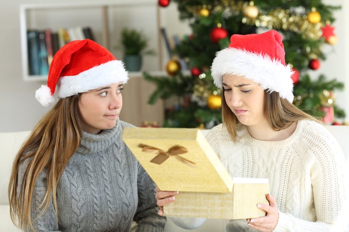 A woman makes a face as she looks inside a gift box.