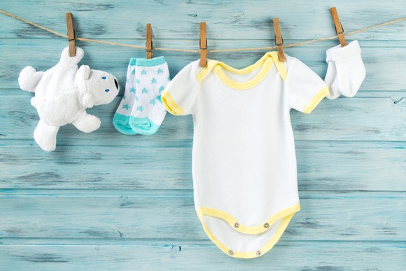 A baby's bodysuit, socks, and stuffed bear hang on a clothes line.