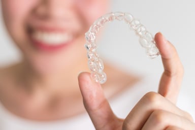 Smiling woman holding clear aligner