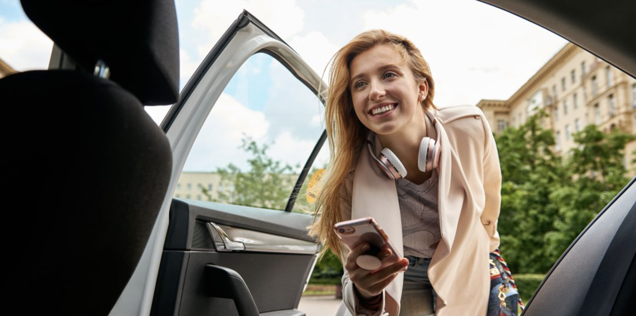 A woman holding a smartphone getting into a car
