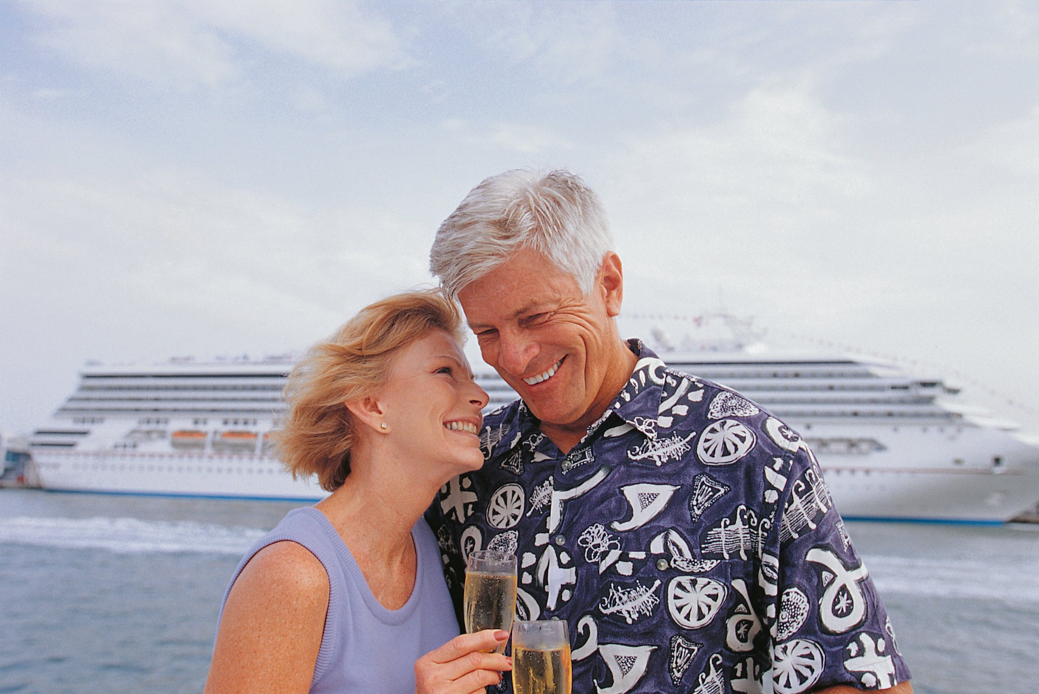 An older couple smiling in front of a cruise ship