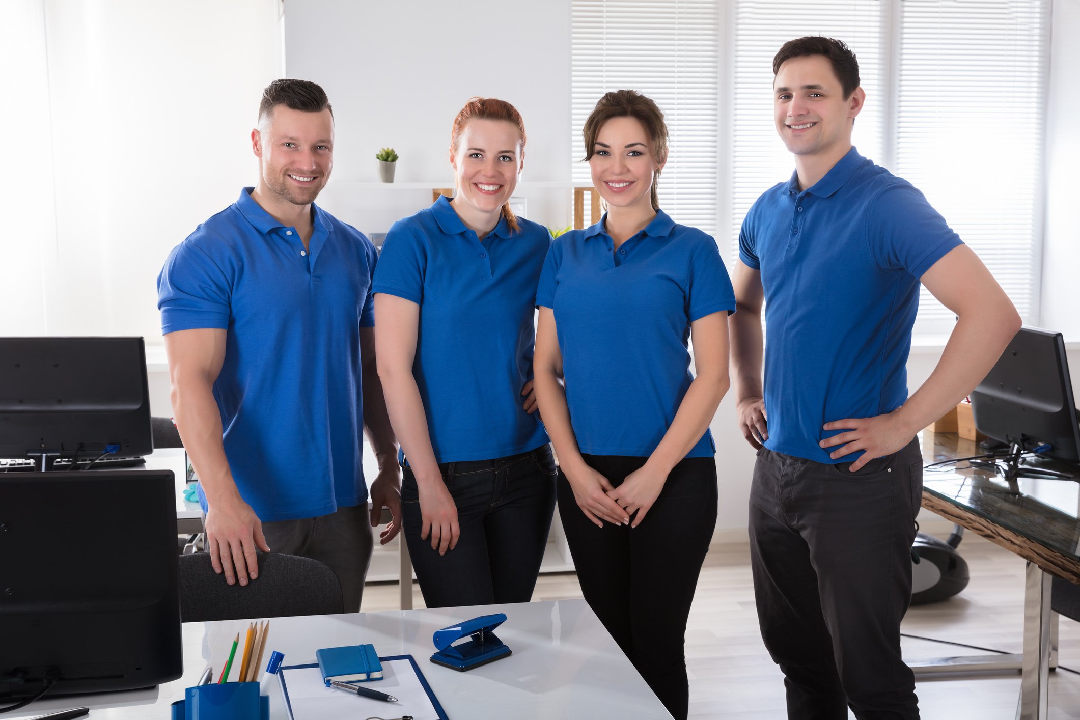 Four janitors in blue uniforms pose in an office space.