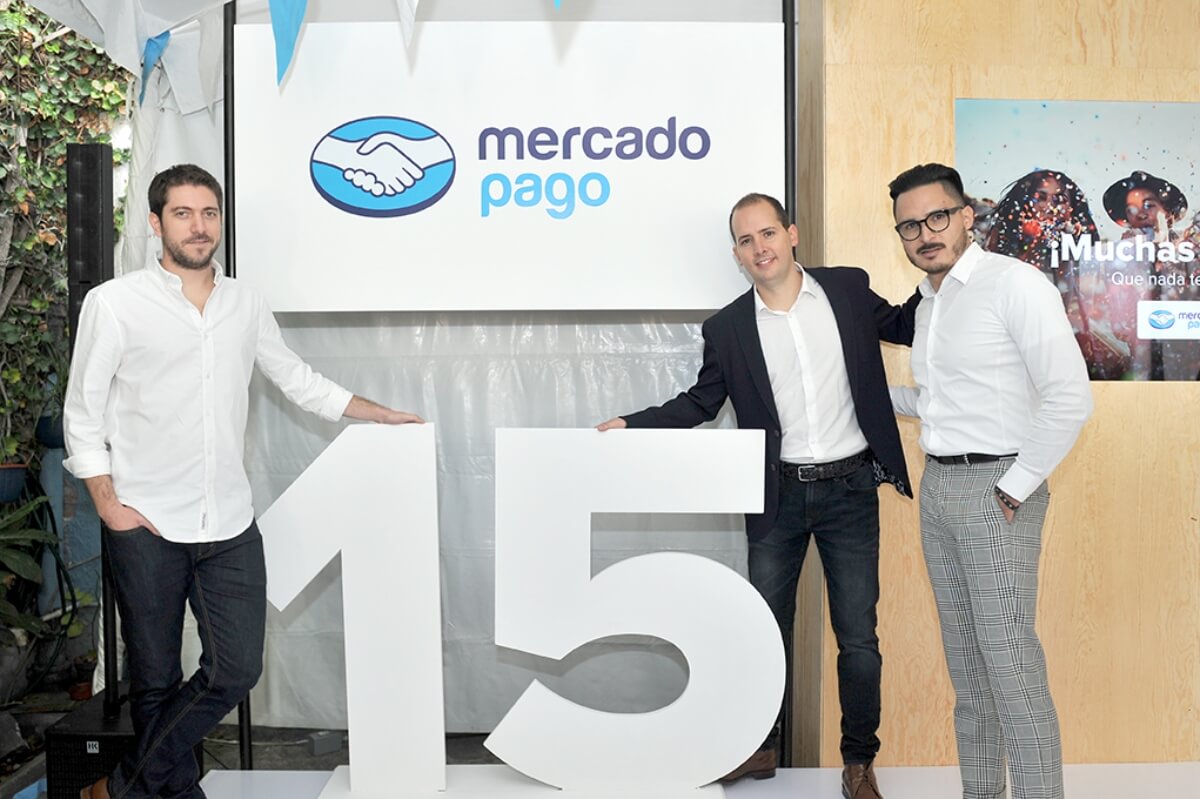 Three people in front of a Mercado Pago banner and the number 15.