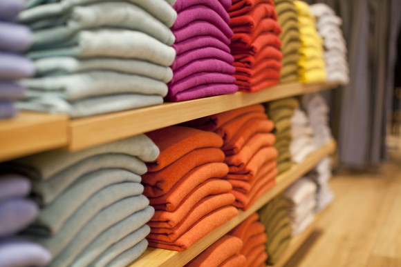 Sweaters in pink, orange, and yellow folded on two shelves in a store. 