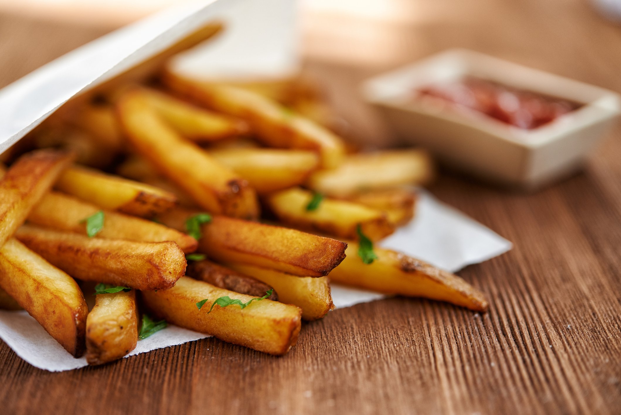 Close-up shot of some golden brown french fries, sprinkled with dill. In the background, you see an out-of-focus ketchup container.